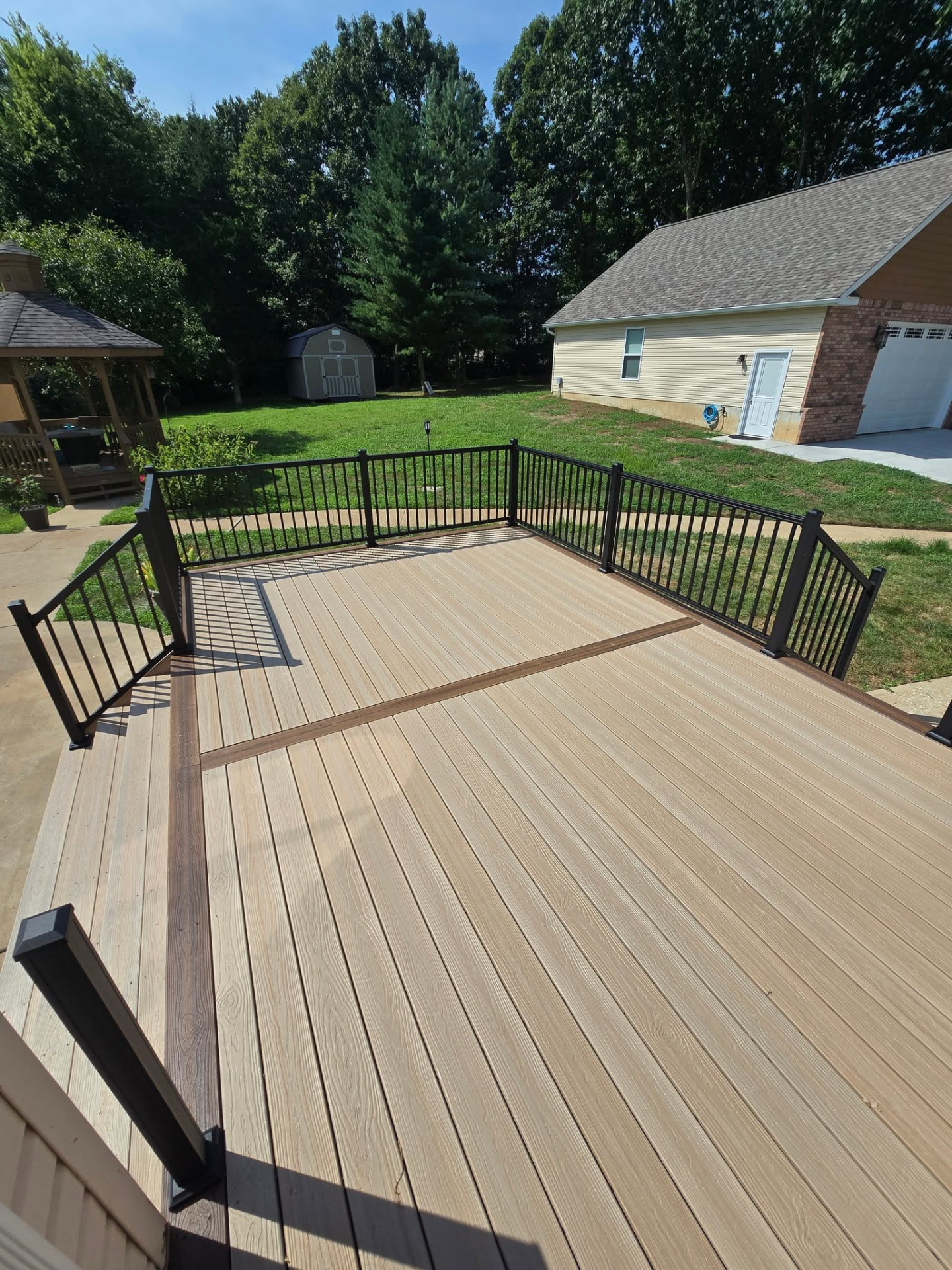 Composite deck with contrasting picture-frame border, double dividers, and black aluminum handrails by B&R Construction